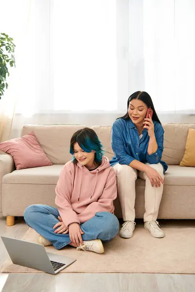 Asian mother and daughter in casual wear, seated on a couch, engaged in separate digital world — Stock Photo