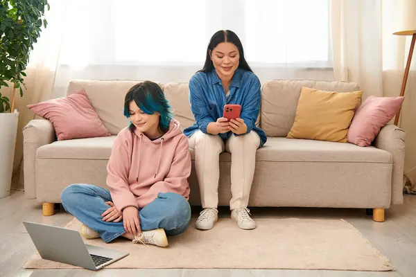 Mère asiatique et sa fille adolescente, portant des vêtements décontractés, sont assis sur un canapé et se concentrent sur un écran de téléphone portable. — Photo de stock