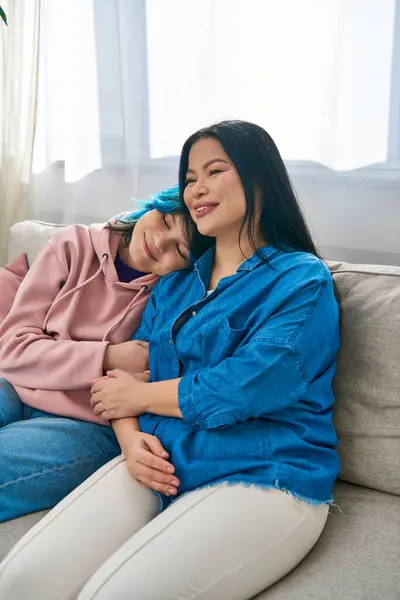 Une mère asiatique et sa fille adolescente en tenue décontractée s'assoient ensemble sur un canapé, partageant un moment de proximité. — Photo de stock