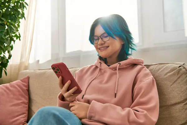 Asian teenage girl in casual wear sitting on a couch, engrossed in cell phone — Stock Photo