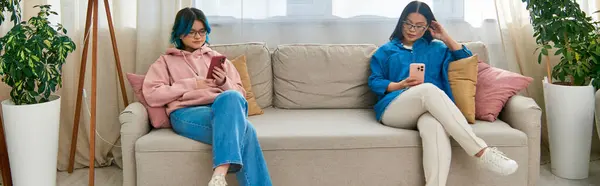 Asian mother and teenage daughter sitting on a couch, sharing a peaceful moment in front of a window. — Stock Photo