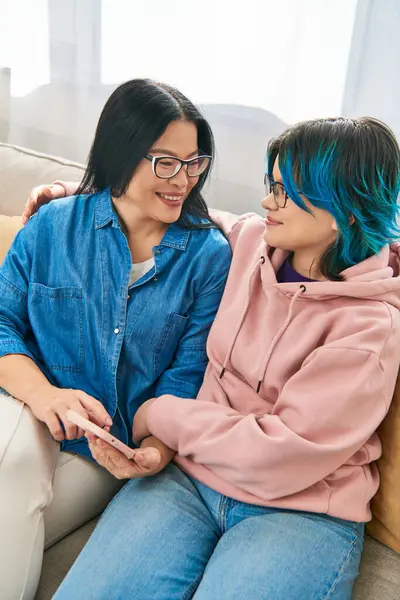 Une mère asiatique et sa fille adolescente se détendent confortablement sur un canapé en tenue décontractée, partageant un moment paisible à la maison. — Photo de stock