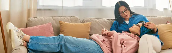 Азіатська мати і її дочка-підліток сидять на дивані, насолоджуючись затишною миттю вдома. — стокове фото