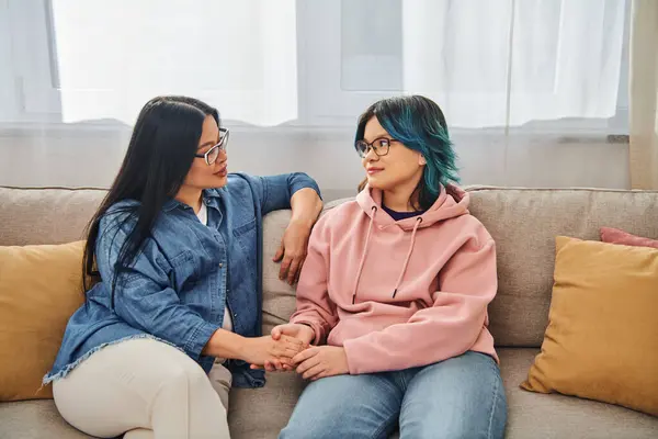 Une mère asiatique et sa fille adolescente en tenue décontractée engagent une conversation profonde tout en étant assise sur un canapé confortable. — Photo de stock