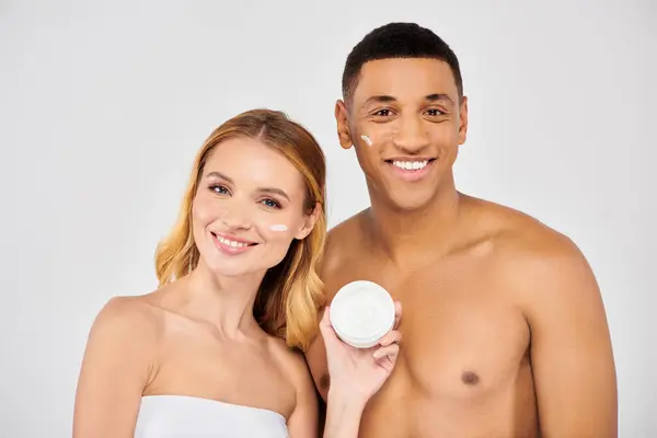 A trendy, diverse couple poses lovingly while applying facial cream. — Stock Photo