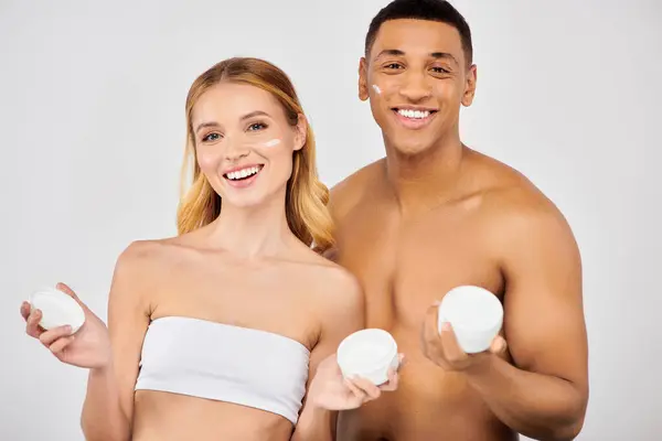Homem e mulher na moda segurando produtos de cuidados da pele juntos. — Fotografia de Stock