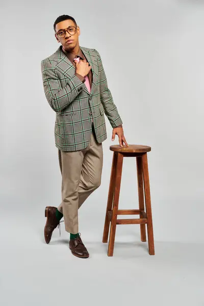 Fashionable man stands by a stool in a plaid blazer. — Stock Photo