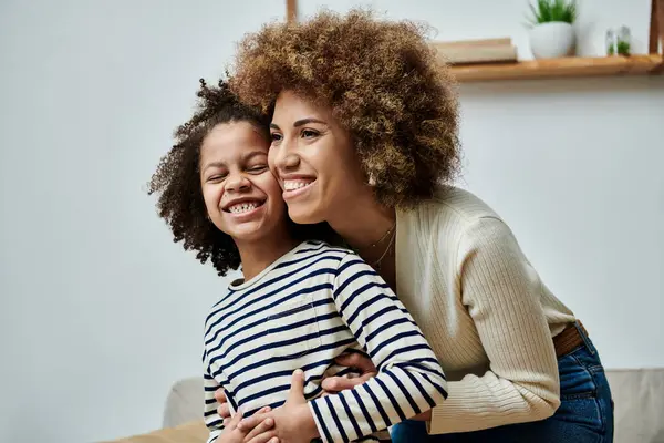 Une mère et une fille afro-américaines heureuses embrassent affectueusement sur un canapé confortable à la maison. — Photo de stock