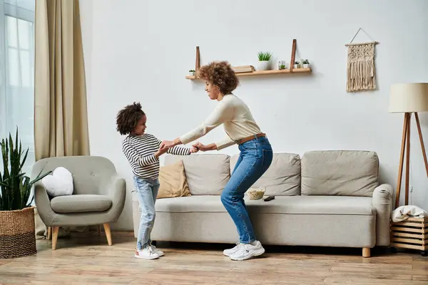 Una madre e una figlia afroamericana ballano gioiosamente su un divano nel loro salotto, condividendo un momento speciale insieme.. — Foto stock