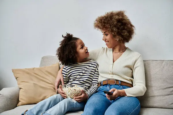 Happy African American mother and daughter sharing a moment on the couch while watching television together. — Stock Photo