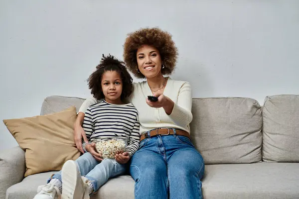 A joyful African American mother and her daughter of African descent sitting on a couch, engrossed in watching television. — Stock Photo