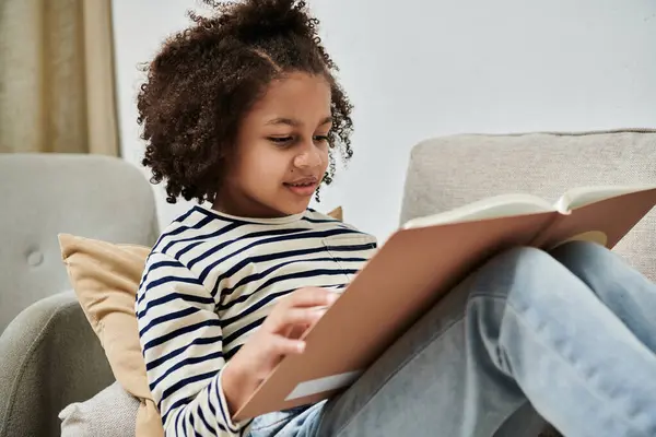Молода дівчина занурилася в книгу, сидячи на затишному дивані — Stock Photo