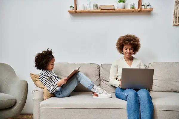 An African American mother and daughter happily seated on a couch, engrossed in using a laptop together. — Stock Photo
