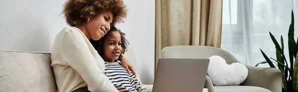Una felice madre e figlia afroamericana sedute su un divano, impegnate con un computer portatile insieme. — Foto stock