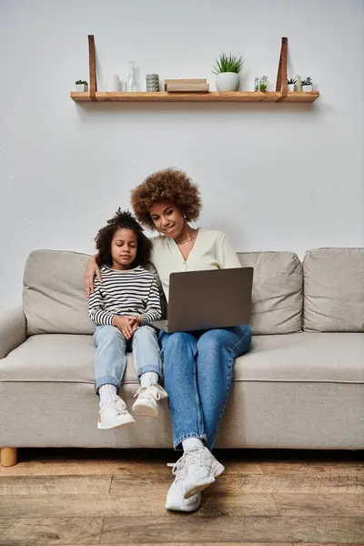 Afroamerikanische Mutter und Tochter benutzen glücklich einen Laptop, während sie zu Hause auf einer Couch sitzen. — Stockfoto