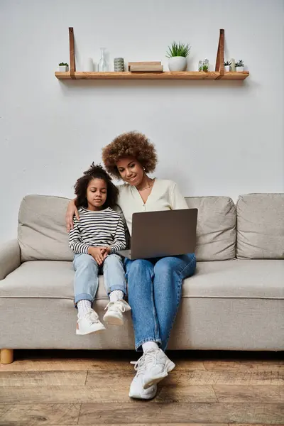 African American mother and daughter happily using a laptop while sitting on a couch at home. — Stock Photo