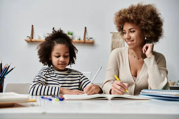 Feliz madre e hija afroamericana compartiendo un momento, escribiendo en un cuaderno en casa. - foto de stock