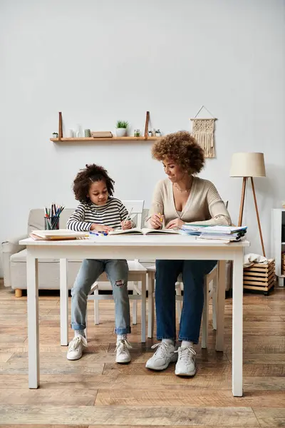 Uma feliz mãe e filha afro-americana sentadas em uma mesa, desfrutando de momentos de qualidade juntos em sua sala de estar. — Fotografia de Stock