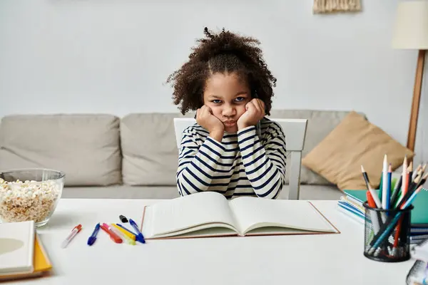 A little girl engrossed in a book at a table, feeling bored — Stock Photo