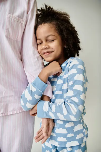 Uma mãe e filha afro-americana vestindo pijama abraçam-se alegremente em um fundo cinza. — Fotografia de Stock
