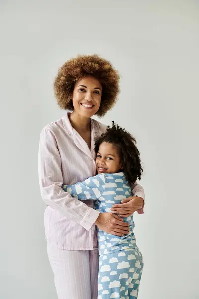 Glückliche afroamerikanische Mutter und Tochter teilen eine herzliche Umarmung in kuscheligen Pyjamas auf grauem Hintergrund. — Stockfoto