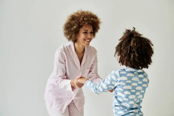 An African American mother and daughter in pajamas shake hands, radiating warmth and unity against a grey background. — Stock Photo