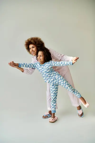 A happy African American mother and daughter in matching pajamas, posing together on a grey background. — Stock Photo