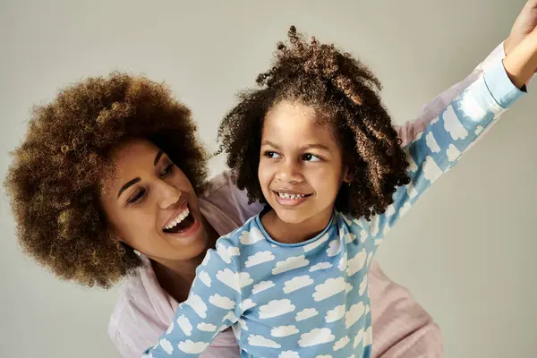 Happy African American mother and daughter in pajamas, enjoying quality time together on a grey background. — Stock Photo
