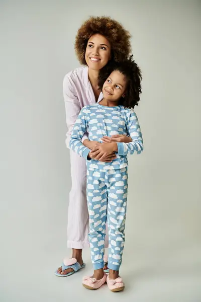 Uma alegre mãe e filha afro-americana fazem uma pose em pijama combinando com um pano de fundo cinza. — Fotografia de Stock