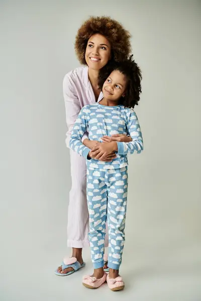 Une joyeuse mère et fille afro-américaine posent en pyjama assorti sur fond gris. — Stock Photo