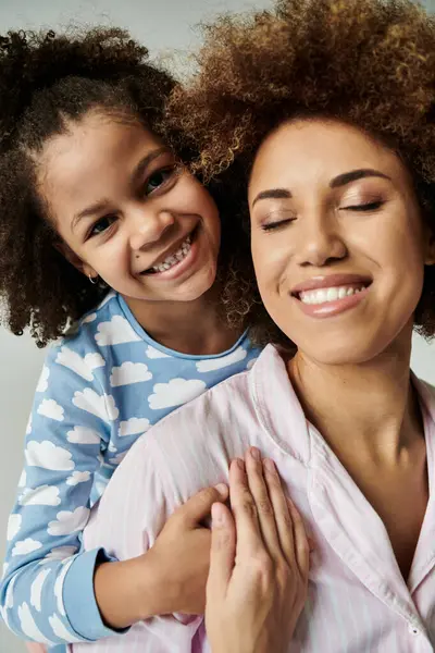 An African American mother and daughter in pajamas smiling happily together against a grey background. — Stock Photo