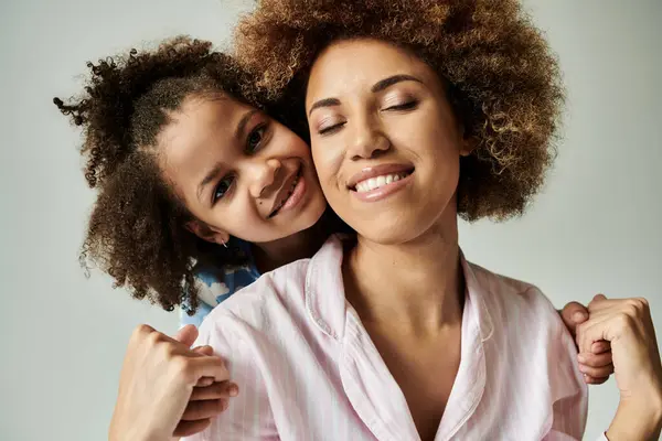 Smiling African American mother and daughter in pajamas, posing happily against a grey background. — Stock Photo
