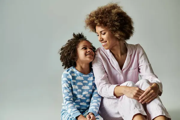 A happy African American mother and daughter in pajamas sitting together on a gray background. — Stock Photo