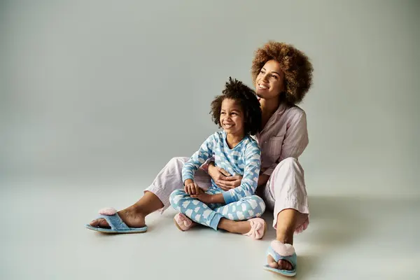 Eine glückliche afroamerikanische Mutter und Tochter sitzen in kuscheligen Pyjamas auf dem Boden und teilen einen besonderen Moment der Bindung. — Stockfoto