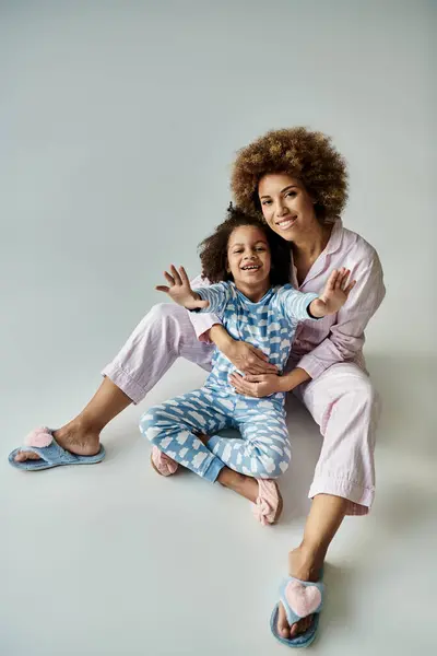 Uma alegre mãe e filha afro-americana em pijama combinando fazem uma pose juntos em um pano de fundo cinza. — Fotografia de Stock