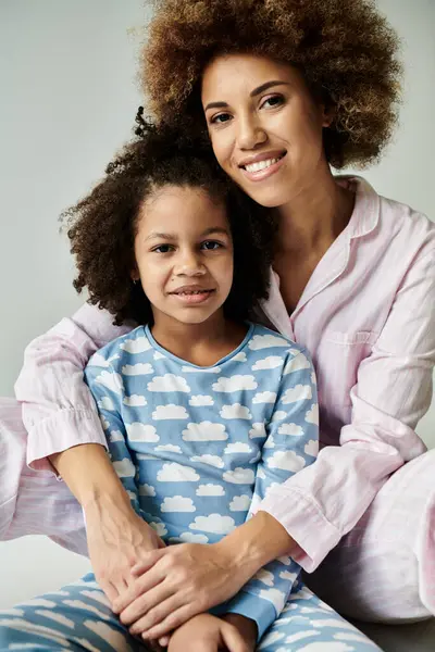 Uma alegre mãe e filha afro-americana posar em pijama combinando em um fundo cinza macio. — Fotografia de Stock