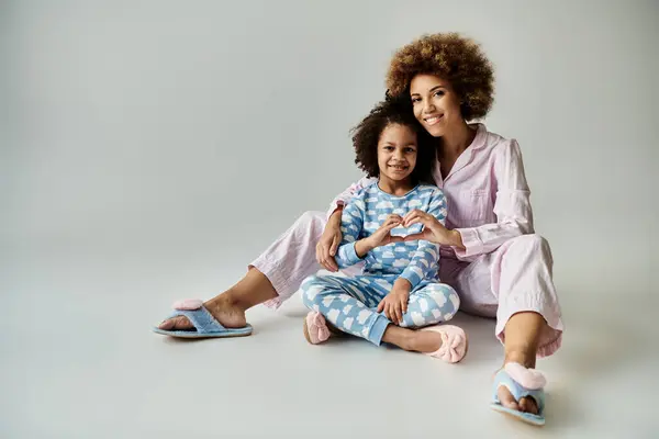 Joyful African American mother and daughter sitting closely on the floor in matching pajamas, sharing a special moment. — Stock Photo