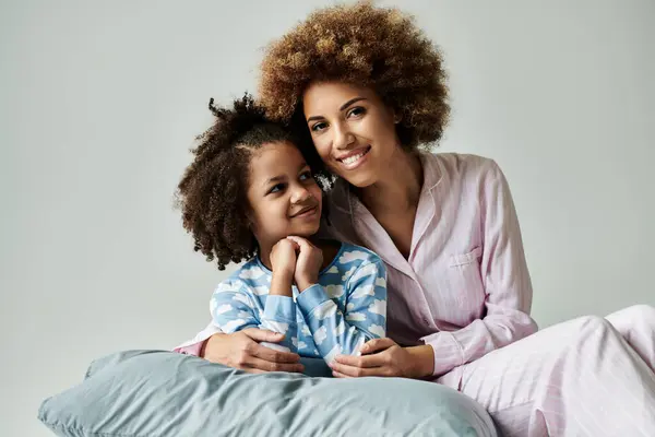 An African American mother and daughter in pajamas happily posing for a photo on a grey background. — Stock Photo