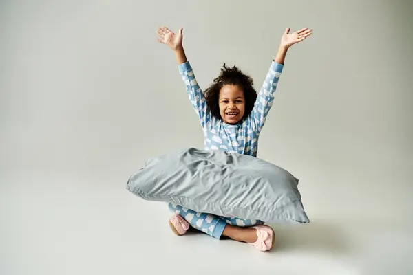 Joyeux enfant afro-américain en pyjama, sur fond gris. La petite fille tient un oreiller. — Photo de stock