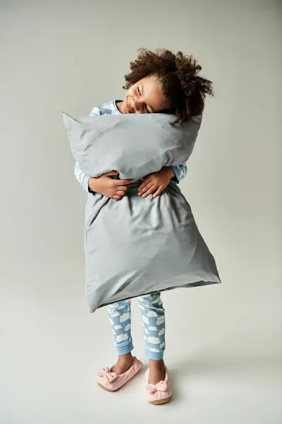 Une jeune afro-américaine en pyjama serre un oreiller dans un moment paisible sur fond gris. — Photo de stock