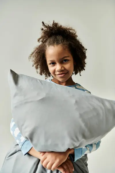 A young girl joyfully hugging a fluffy pillow against a serene white backdrop. — Stock Photo
