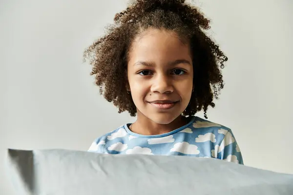 A young girl, dressed in pajamas, playfully hides her face behind a pillow, bringing joy and laughter to the scene. — Stock Photo