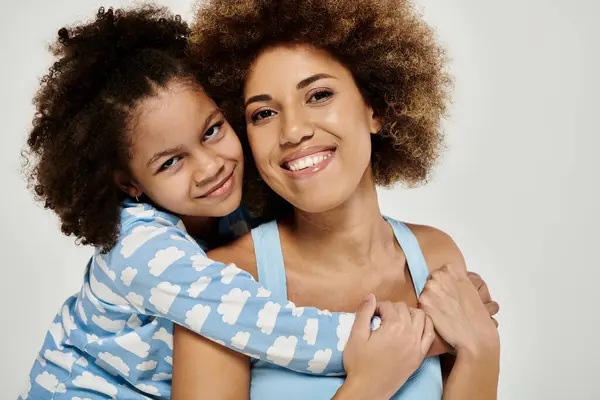 A happy African American mother and daughter in pajamas posing together on a grey background. — Stock Photo