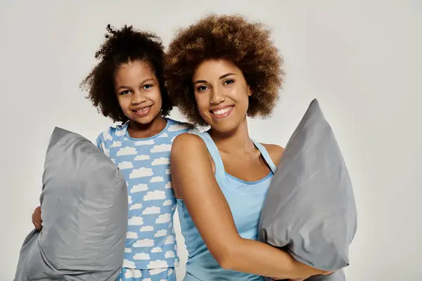 Happy African American mother and daughter in matching pajamas holding pillows on a white background. — Stock Photo