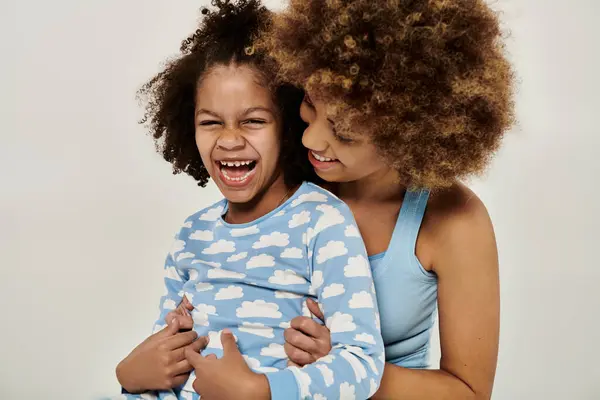 Mãe e filha afro-americana feliz em pijama compartilhando um momento alegre, rindo juntos em um fundo branco. — Fotografia de Stock