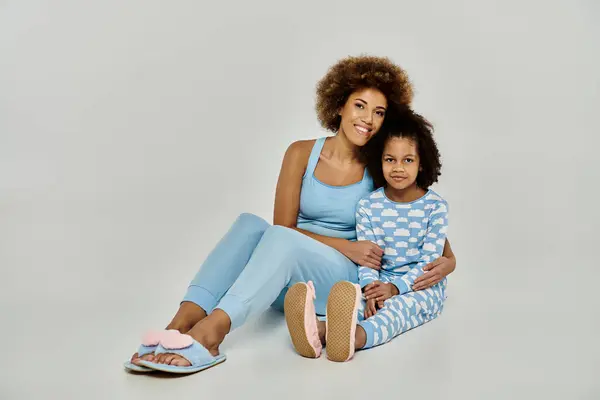 Glückliche afroamerikanische Mutter und Tochter sitzen zusammen im Pyjama auf dem grauen Boden und teilen einen besonderen Moment. — Stockfoto
