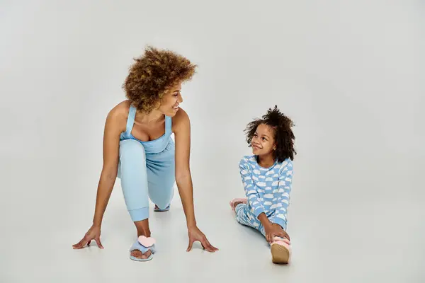 Joyful African American mother and daughter in pajamas practicing yoga together on a peaceful white background. — Stock Photo