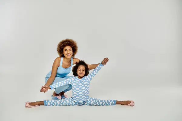 Счастливые афроамериканская мать и дочь в пижаме практикуют йогу вместе на белом фоне. — стоковое фото