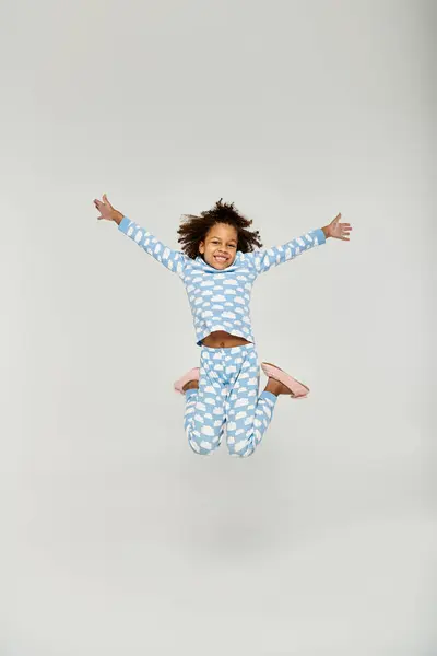 Une jeune afro-américaine saute joyeusement dans les airs, portant un pyjama bleu — Photo de stock