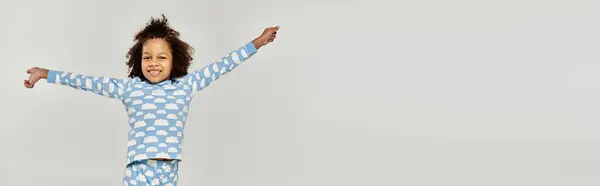 A cheerful African American girl in pajamas extending her arms on a grey background. — Stock Photo